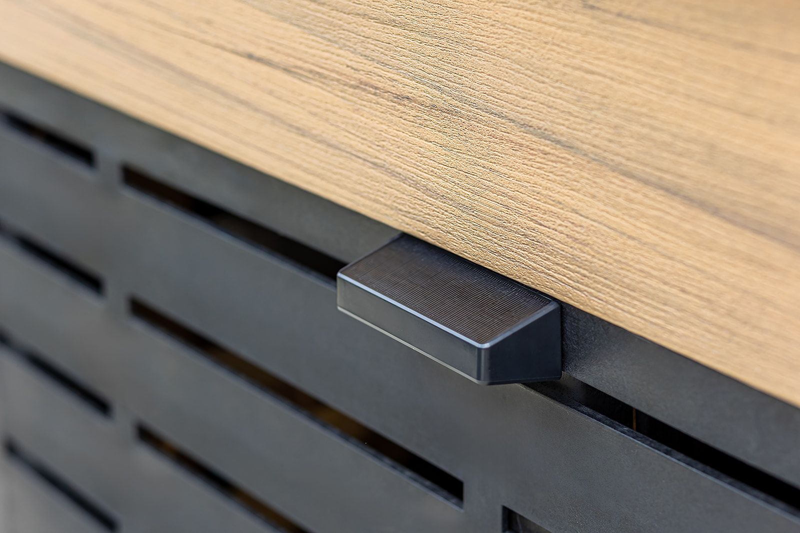 Gros plan sur un plateau de table en bois avec une poignée de tiroir en métal noir. Un panneau avant noir ajouré se trouve sous la table.