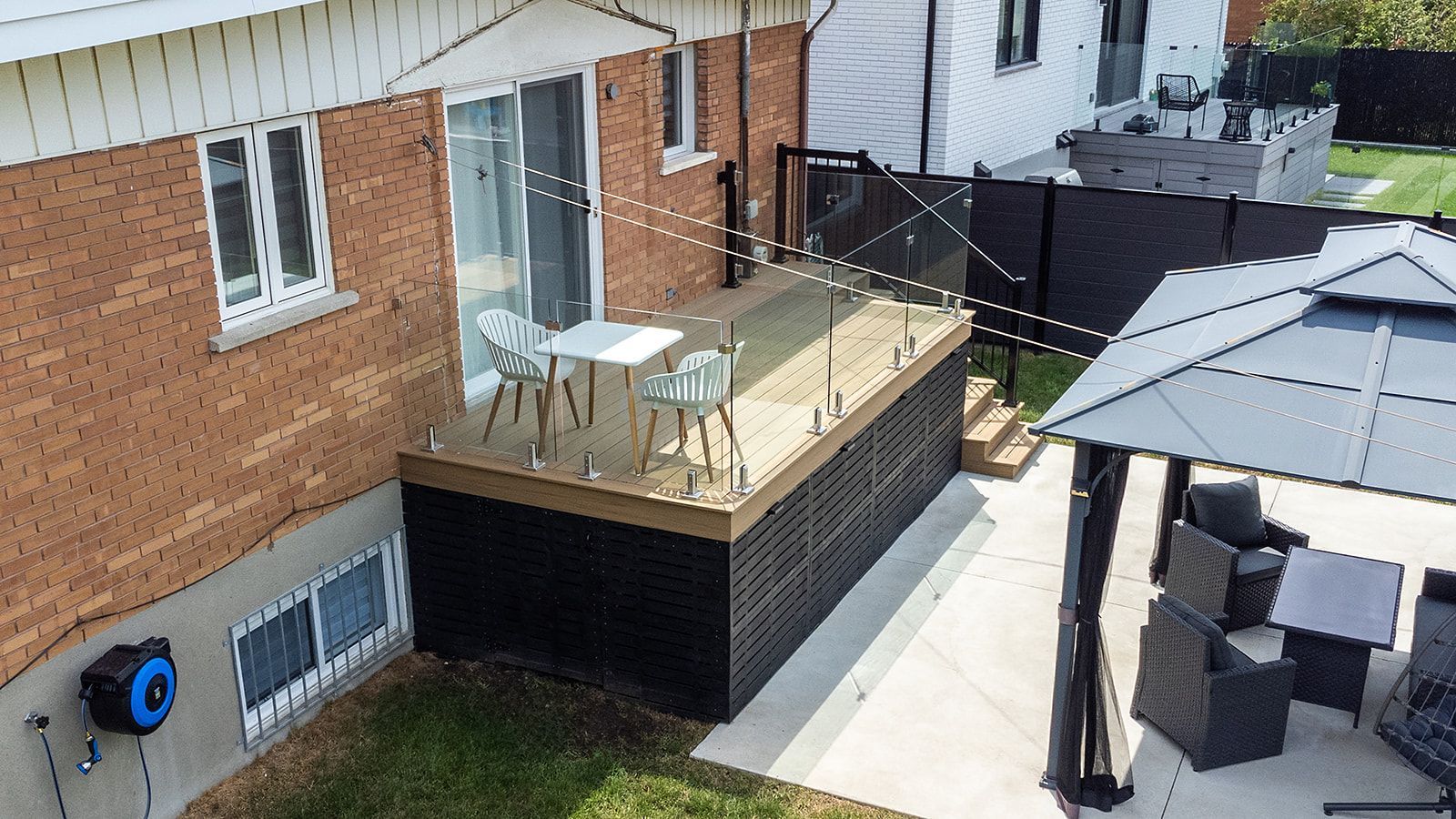 Terrasse arrière avec bordures noires, petite table et chaises, adjacente à une maison en briques et un kiosque.