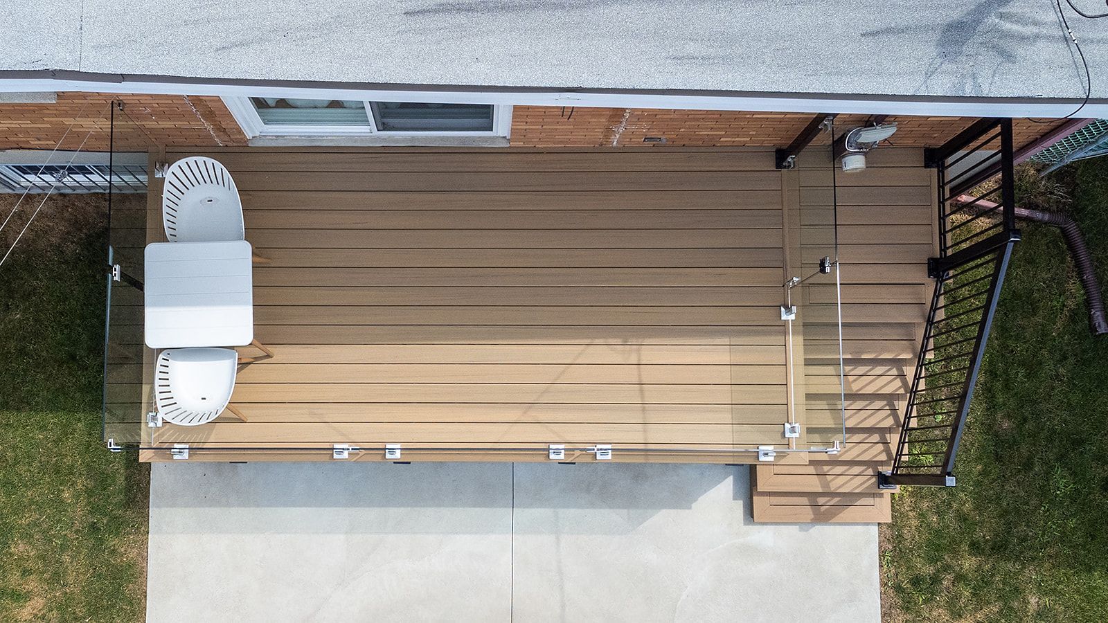 Vue aérienne d'une terrasse composite avec chaise blanche, rambarde et escalier descendant vers une terrasse en béton.