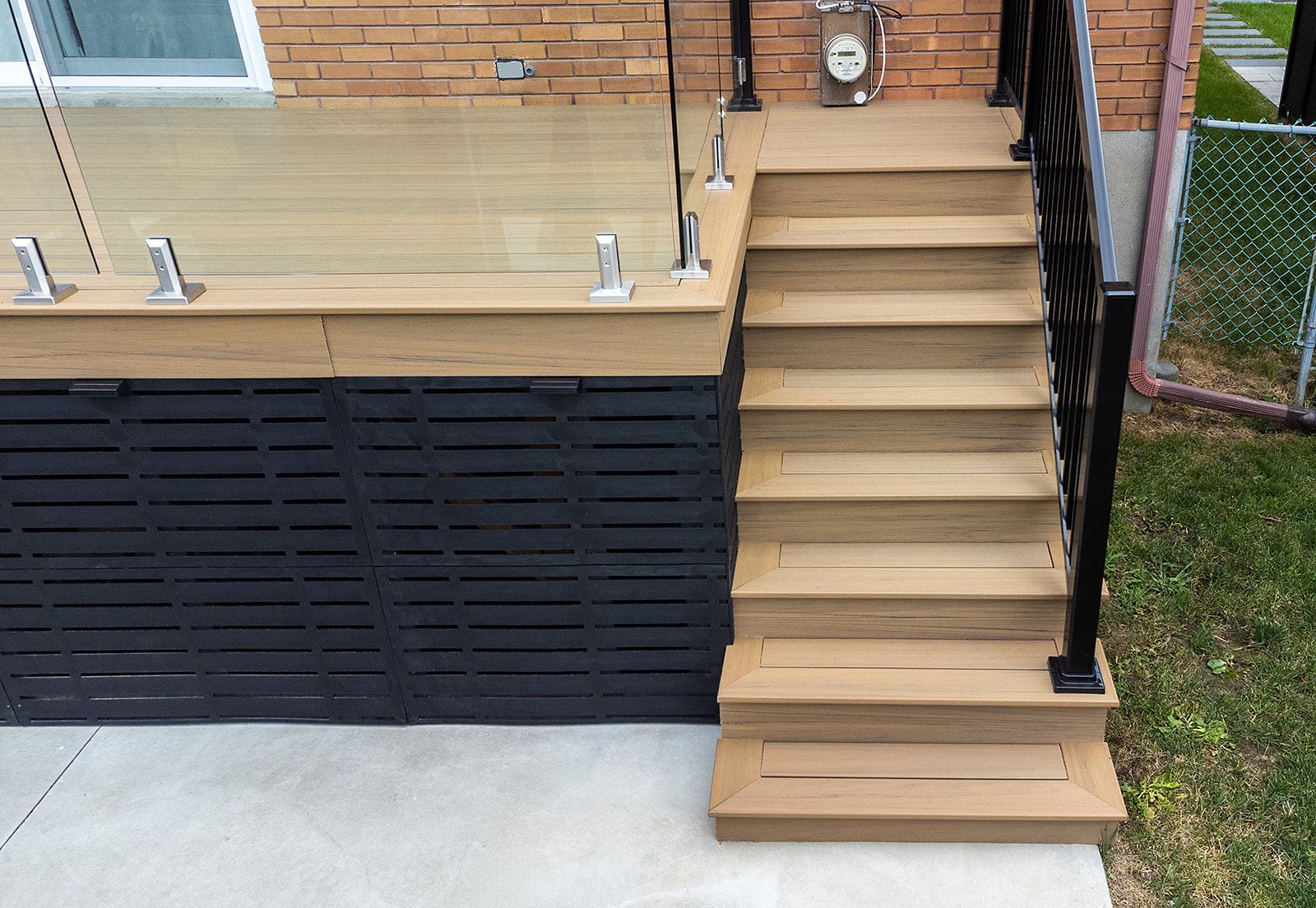 Terrasse en bois avec escalier, rambarde noire et panneaux de verre.