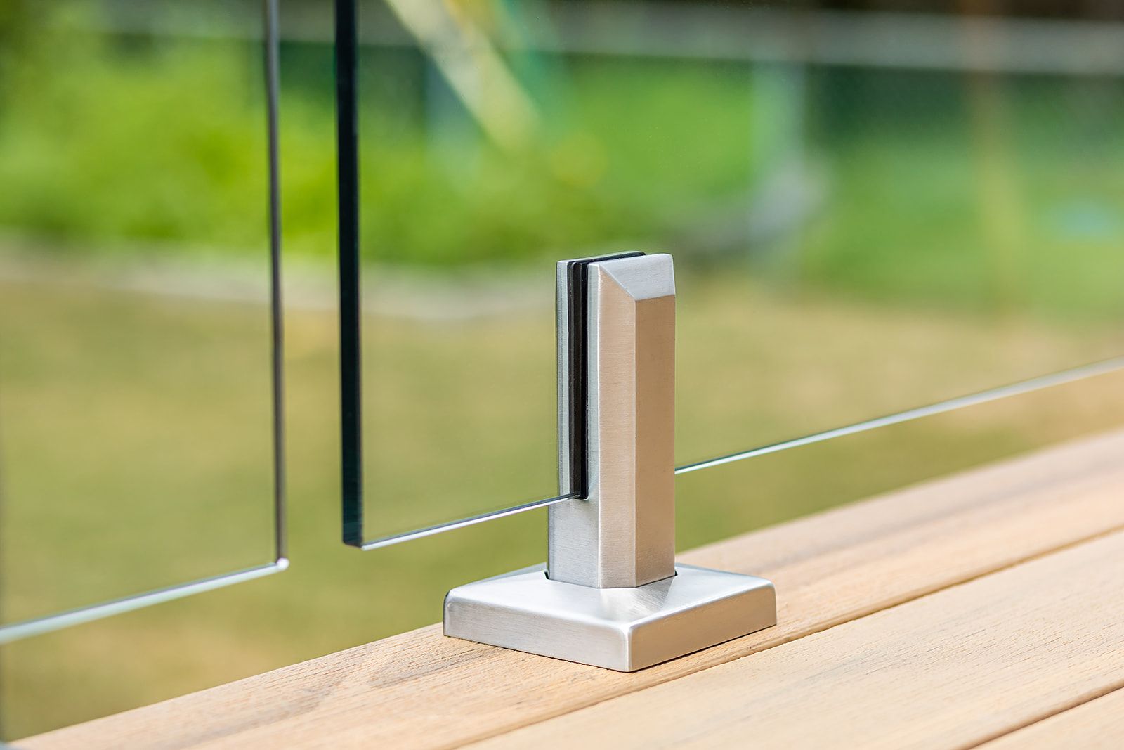 Un poteau de garde-corps en verre avec panneau de verre sur une terrasse en bois. À l'arrière-plan, des arbres verts flous.