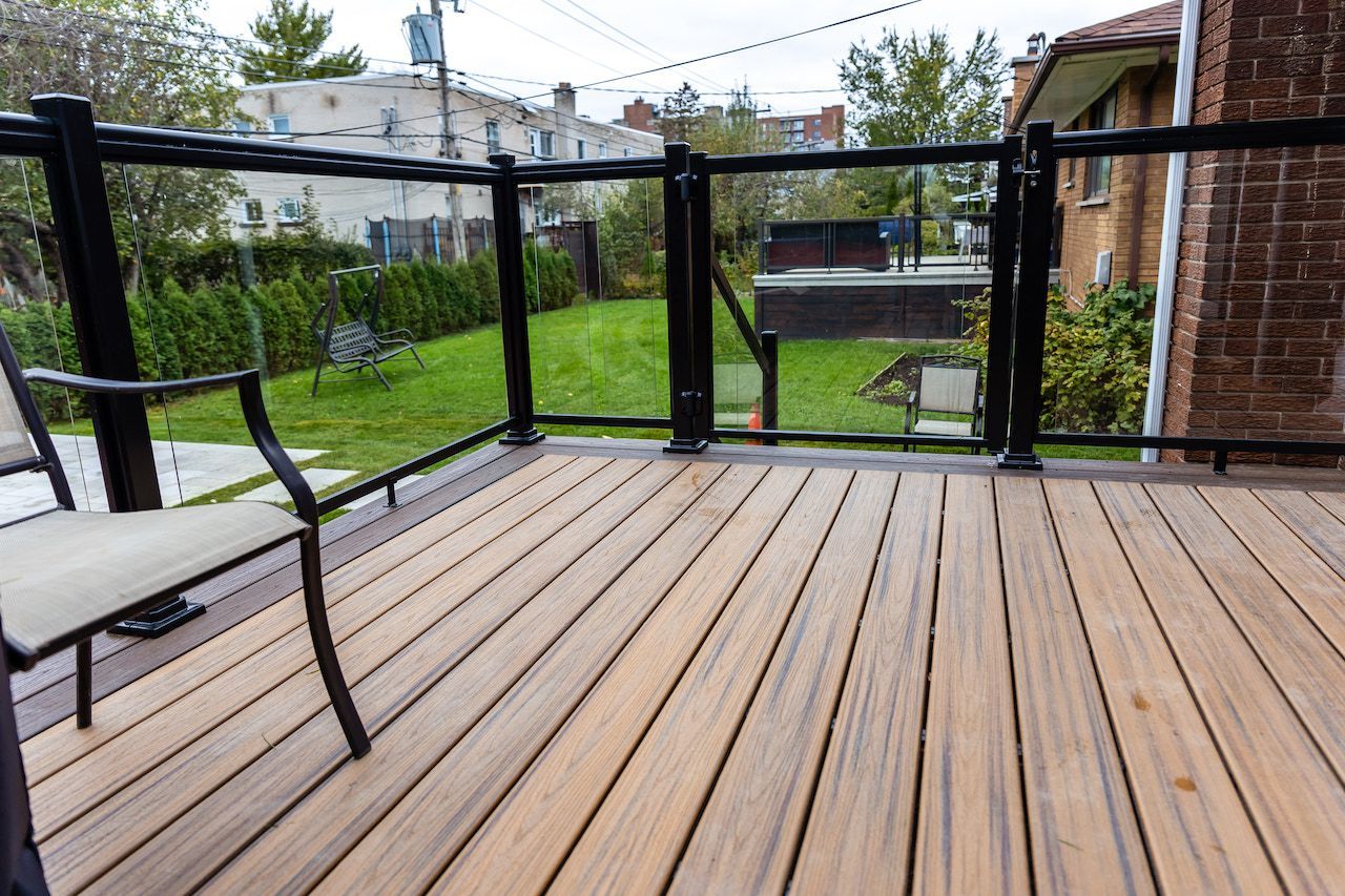 Terrasse en bois avec rambarde noire et panneaux de verre, donnant sur un jardin avec pelouse verte.