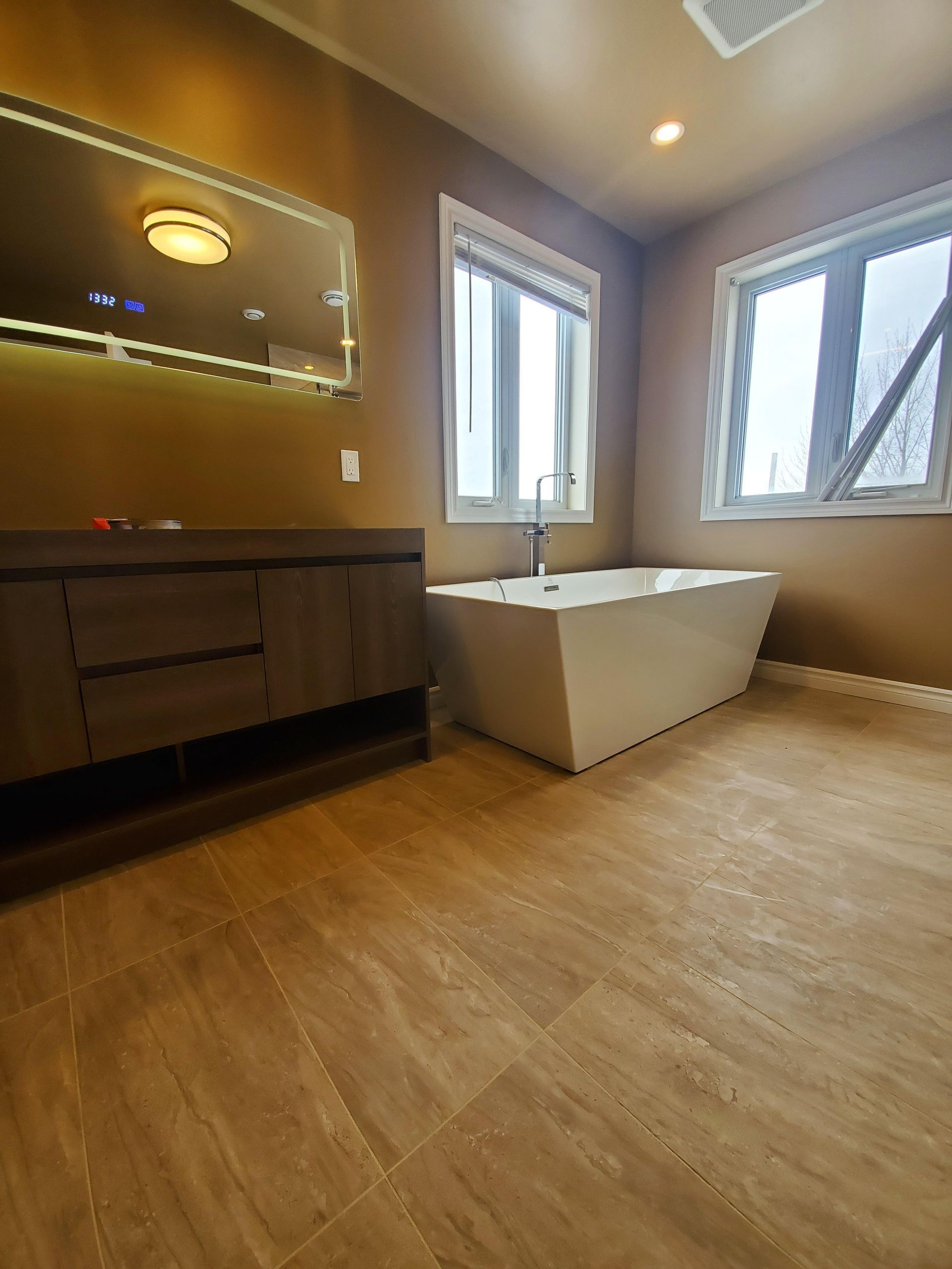 Salle de bains avec baignoire blanche moderne, meuble-lavabo en bois et deux fenêtres.