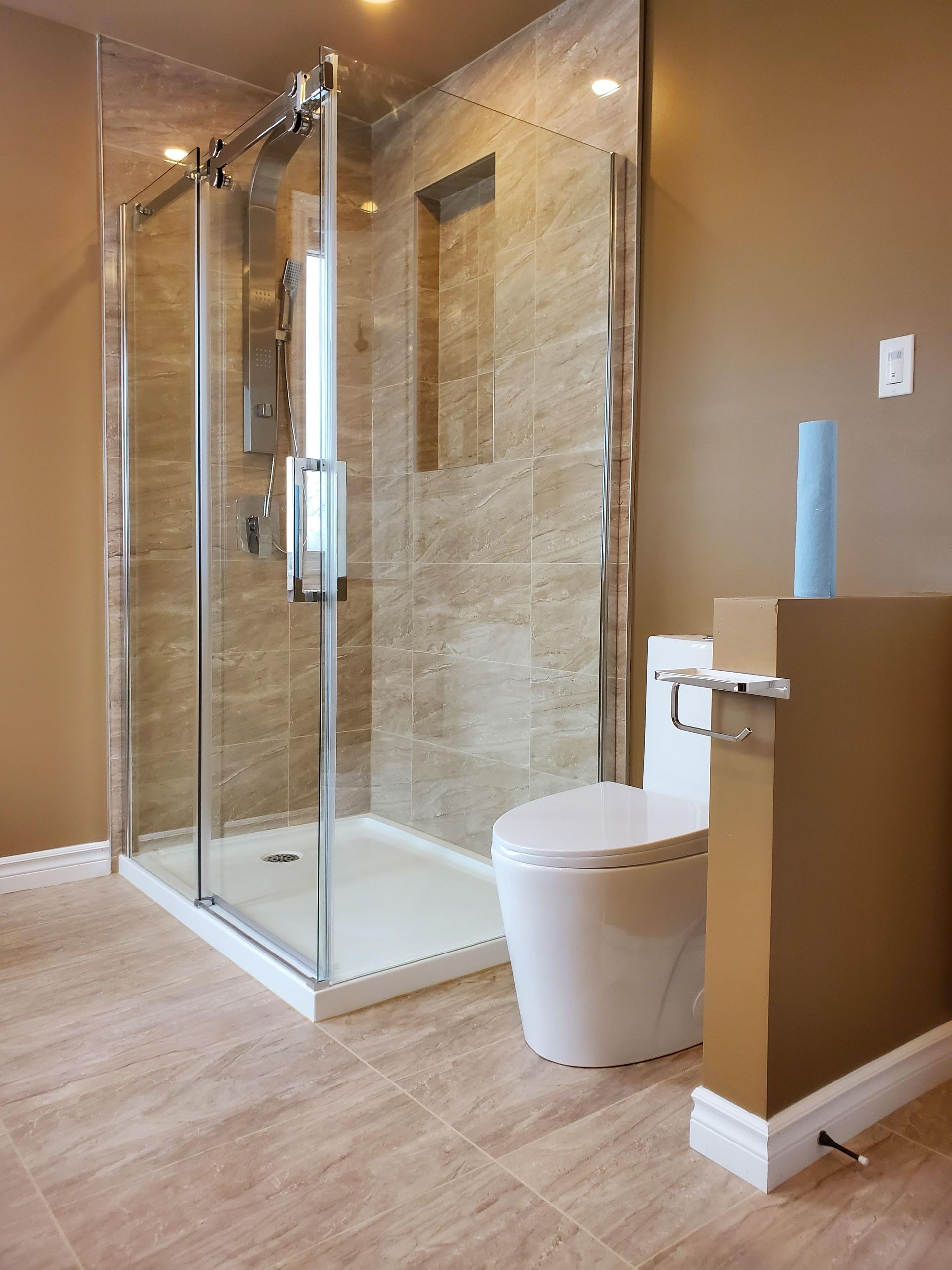 Salle de bains moderne avec douche en verre, toilettes et murs beiges.