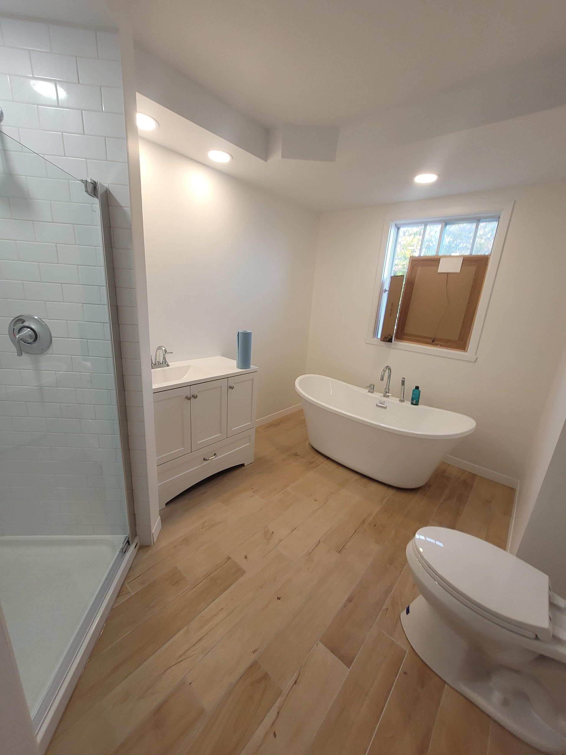 Salle de bains avec baignoire blanche, meuble-lavabo et toilettes ; sol en bois, douche carrelée.