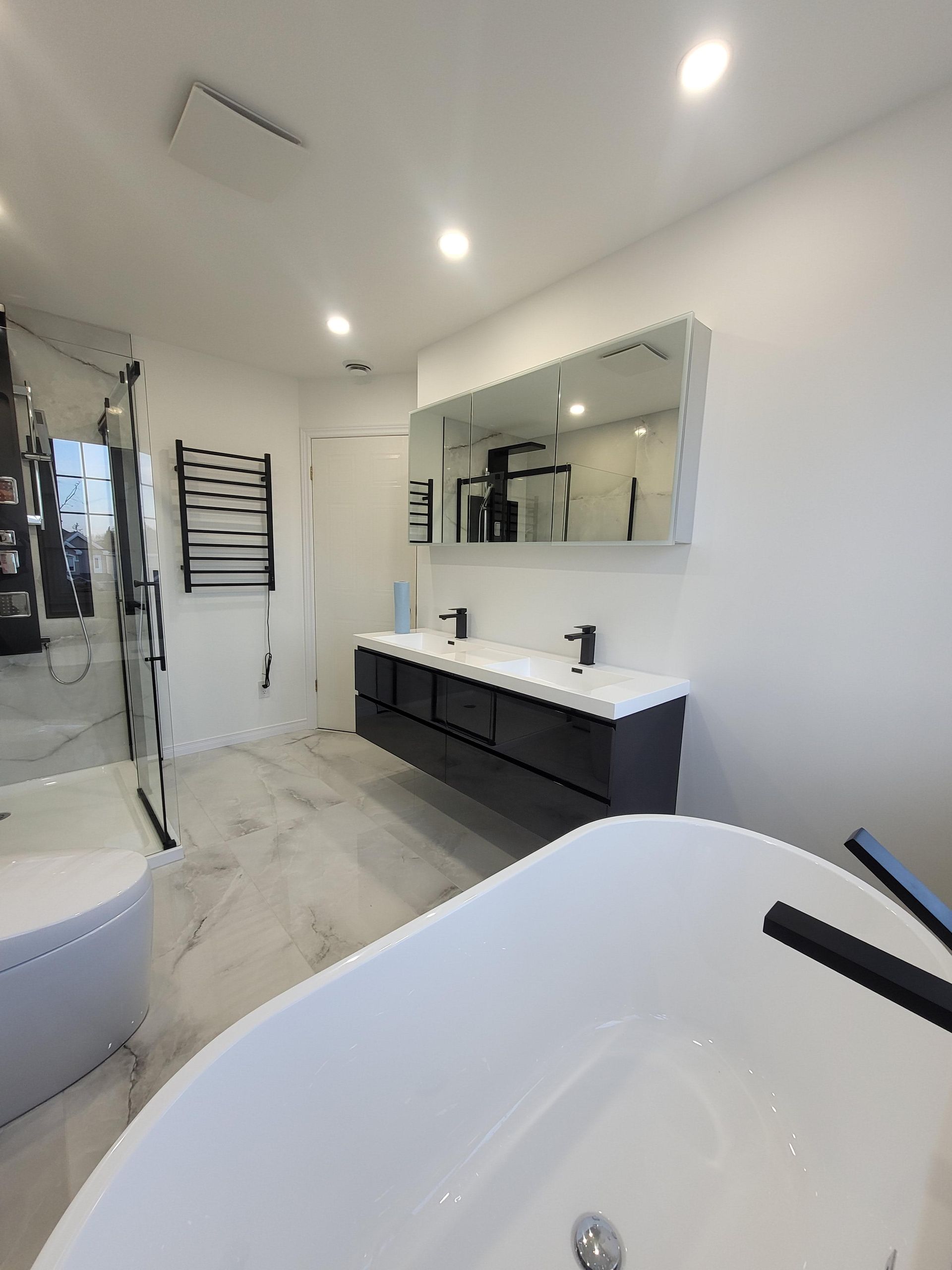 Salle de bains moderne blanche avec un meuble-lavabo suspendu gris foncé, un grand miroir et une baignoire îlot.