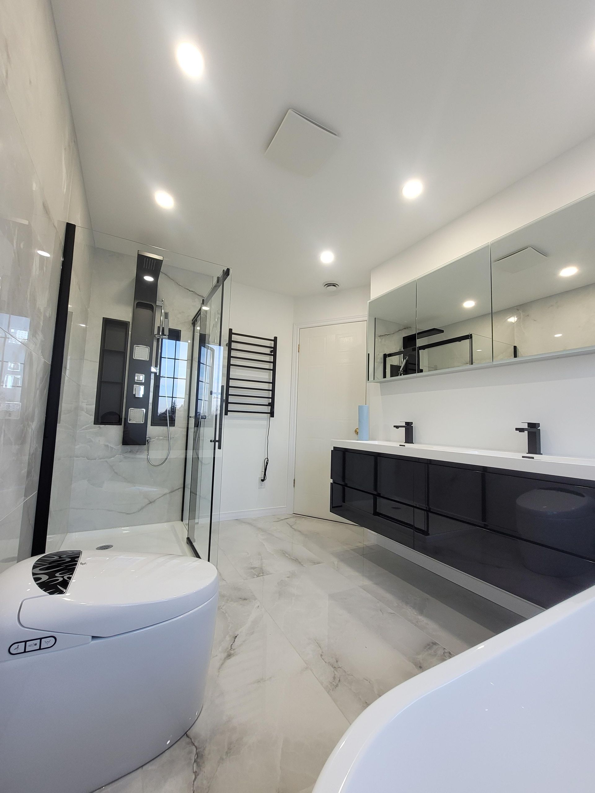 Salle de bains moderne avec murs blancs, touches de noir et un grand miroir au-dessus d'une double vasque.