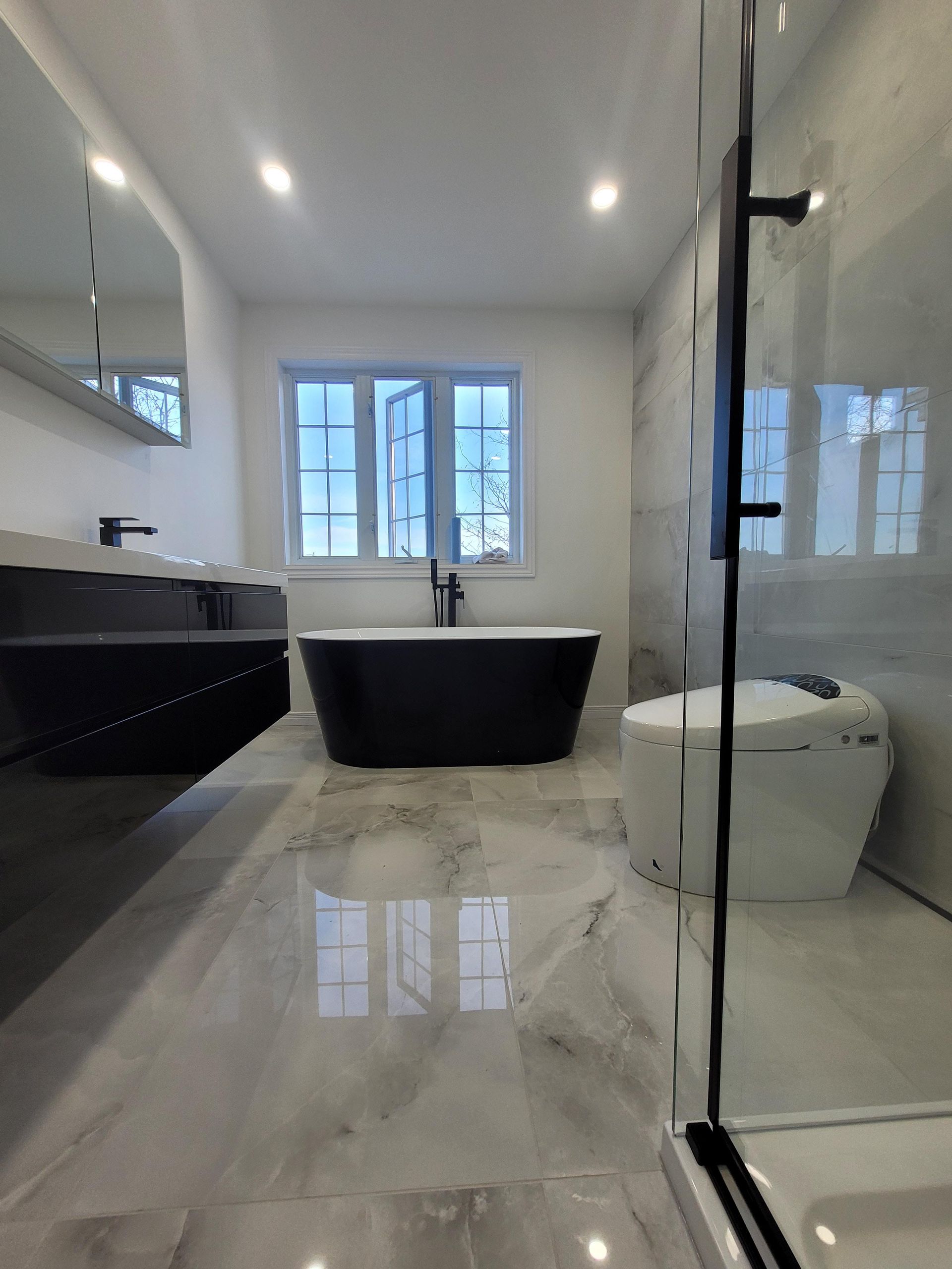 Salle de bains moderne avec baignoire îlot noire, douche en verre et sol en carrelage de marbre.
