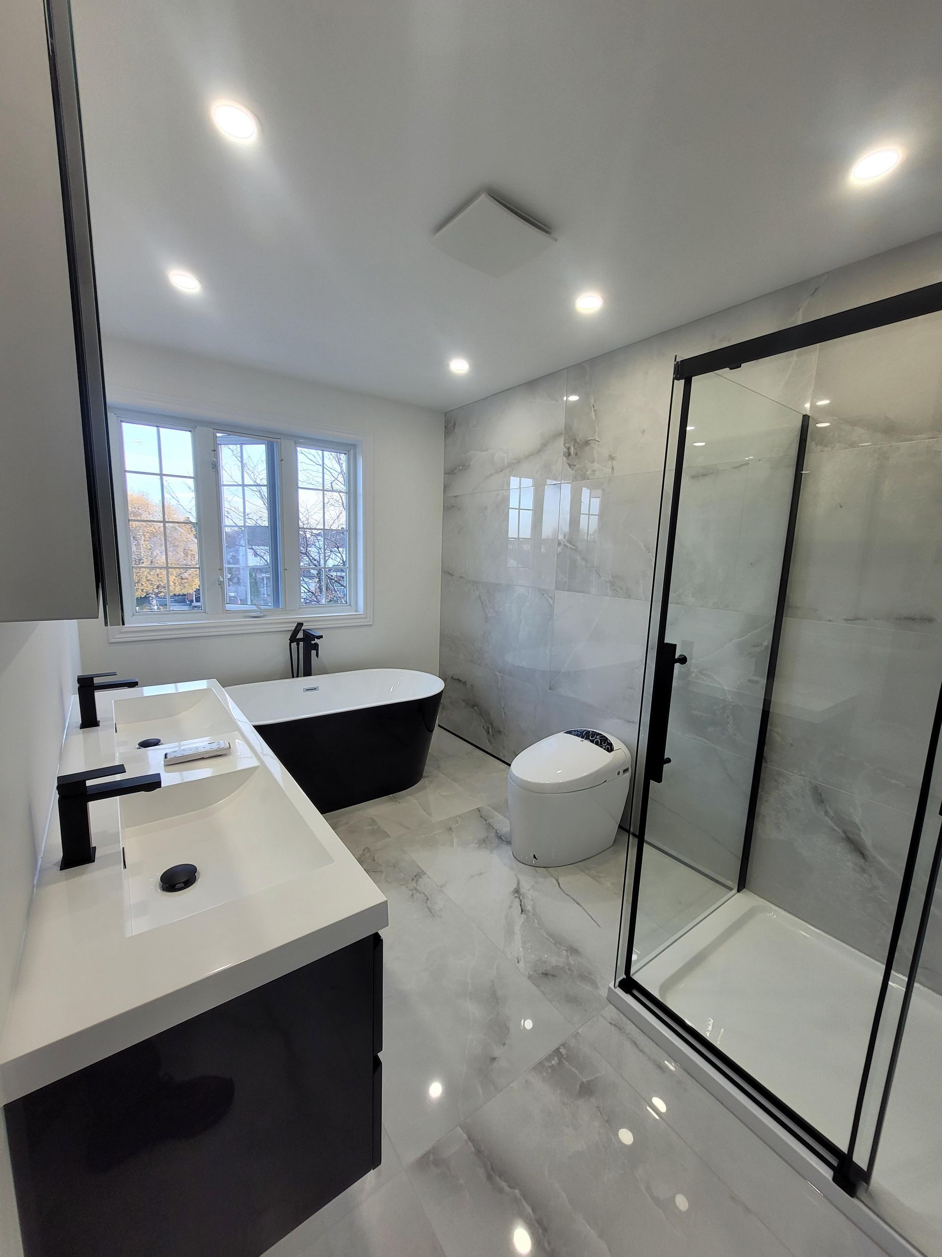Salle de bains moderne avec baignoire noire, meuble-lavabo blanc et carrelage en marbre.