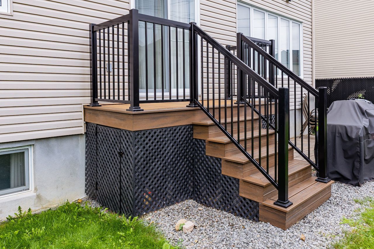 Rambarde et escalier noirs menant à une terrasse attenante à une maison au bardage beige.