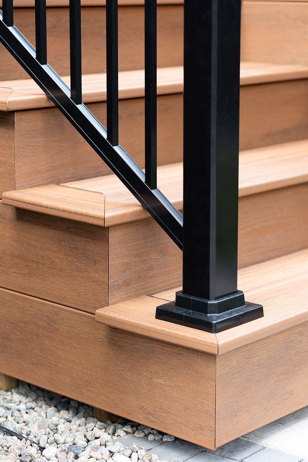 Escalier de terrasse en composite avec poteau de garde-corps noir. Marches et contremarches marron. Base en gravier.