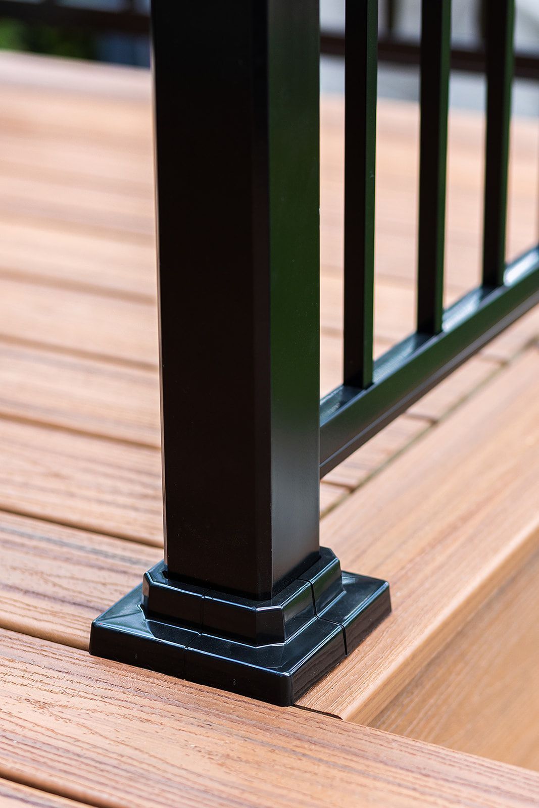 Poteau de rambarde noir sur une terrasse marron avec supports verticaux visibles.