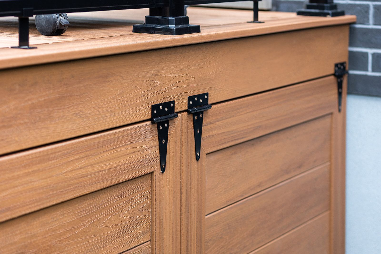 Armoire en bois brun avec charnières et garnitures noires, contre un mur de briques.