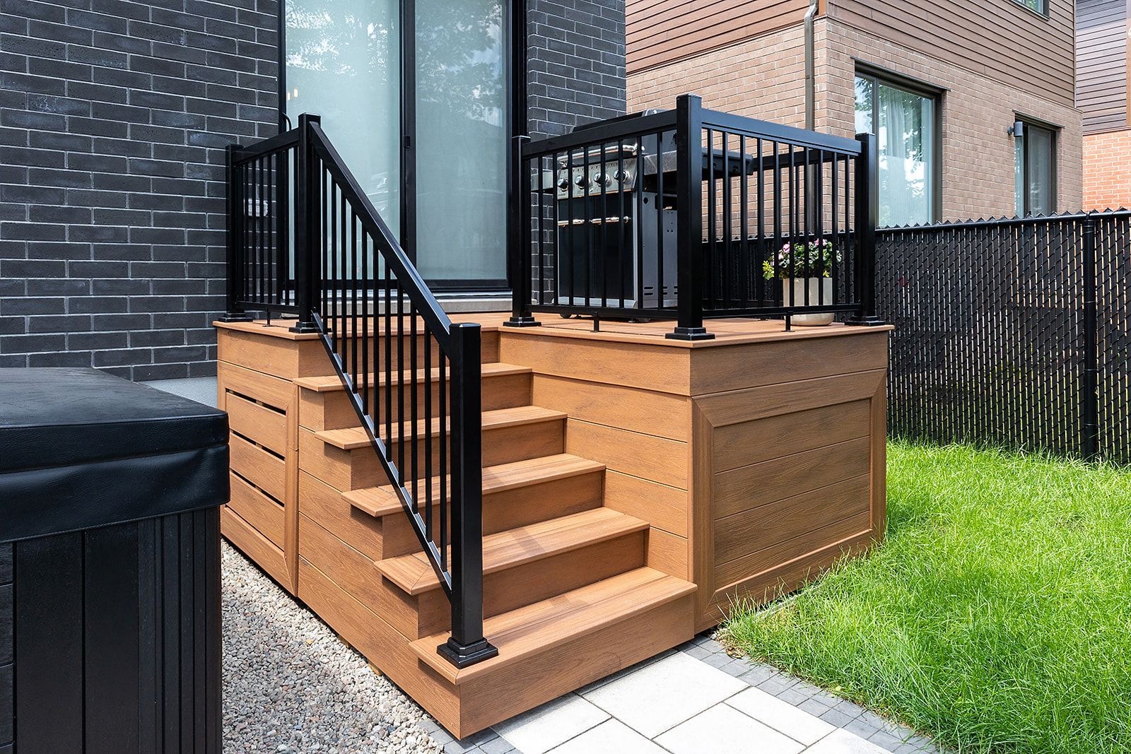 Terrasse en bois avec rambardes noires, escalier et jacuzzi dans un jardin urbain.