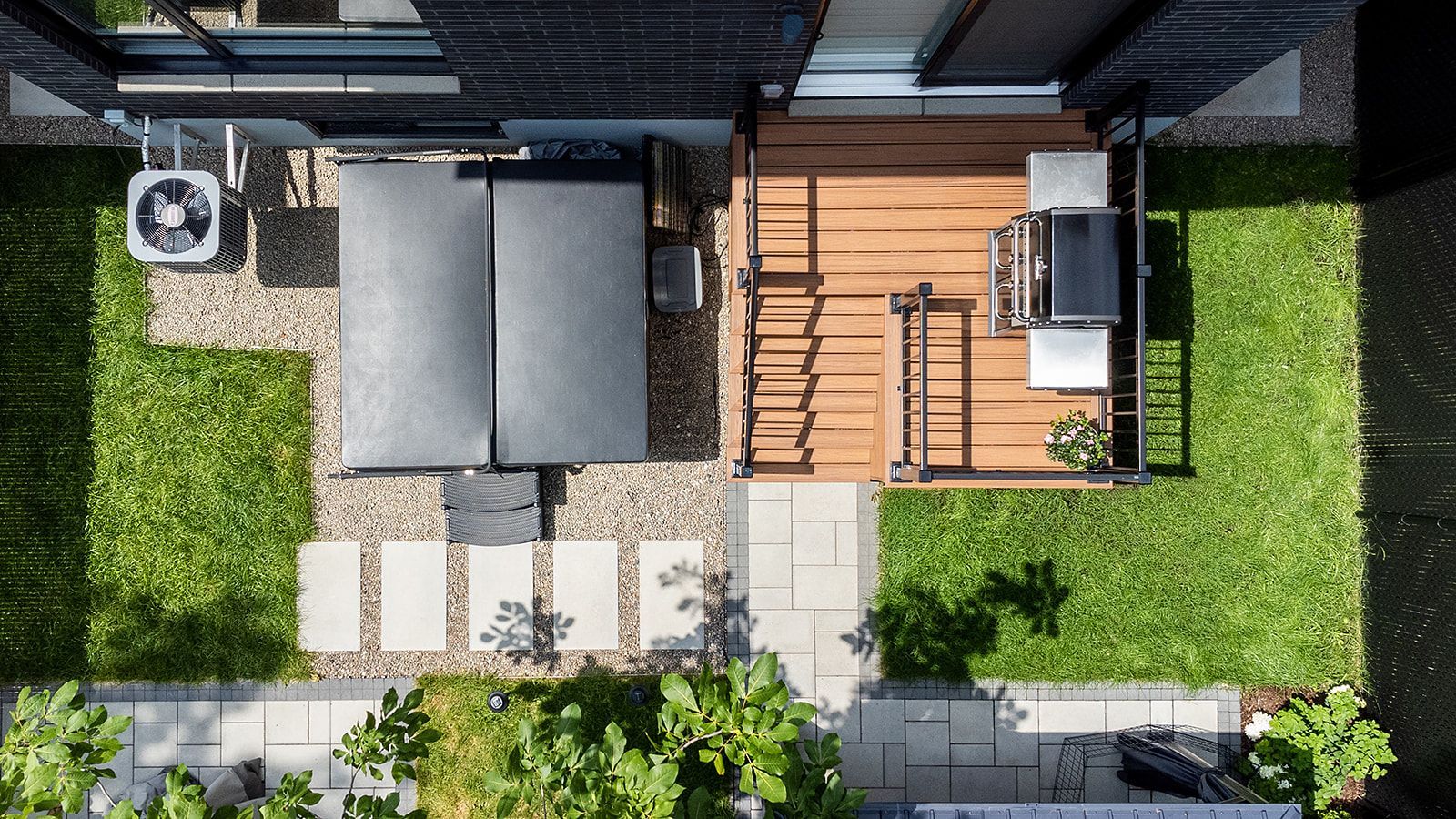 Vue aérienne d'un jardin moderne avec jacuzzi, terrasse en bois, pelouse verte et barbecue.