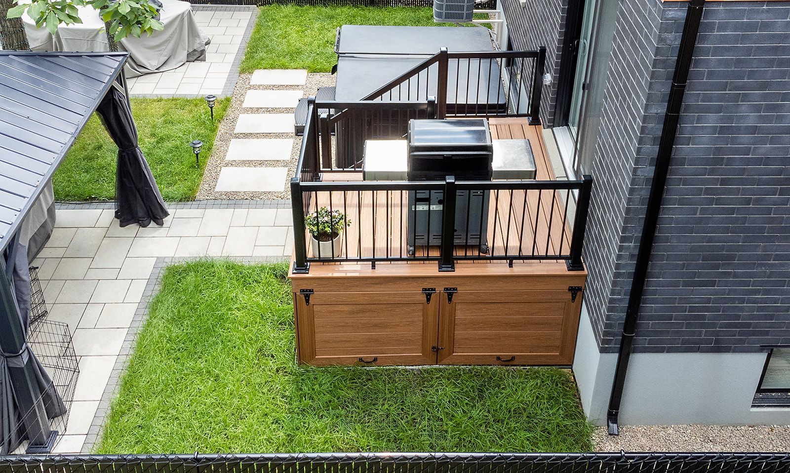 Terrasse arrière avec barbecue intégré, entourée de pelouse et d'un chemin de pierre.