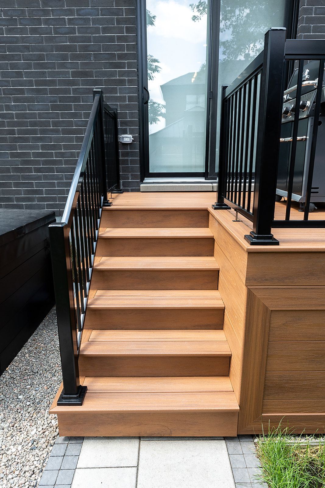 Escalier extérieur en bois avec rampe noire, menant à une porte vitrée.