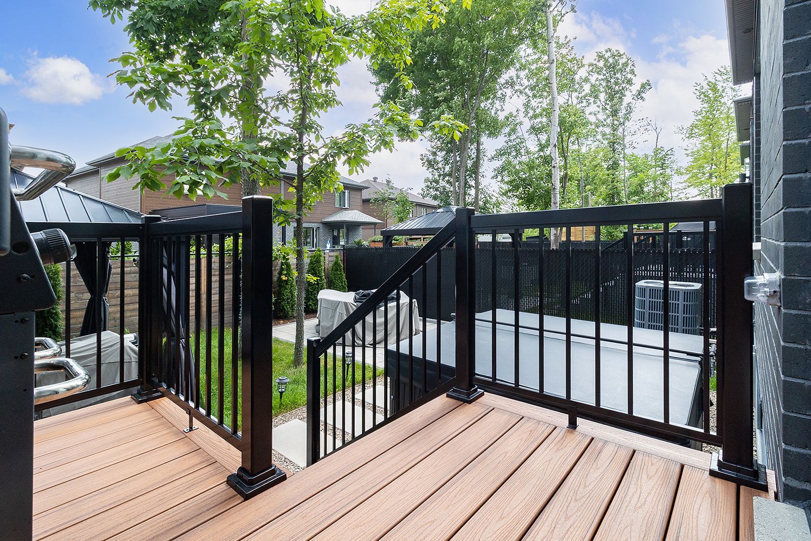 Terrasse en bois avec rambarde noire donnant sur un jardin arboré avec patio.