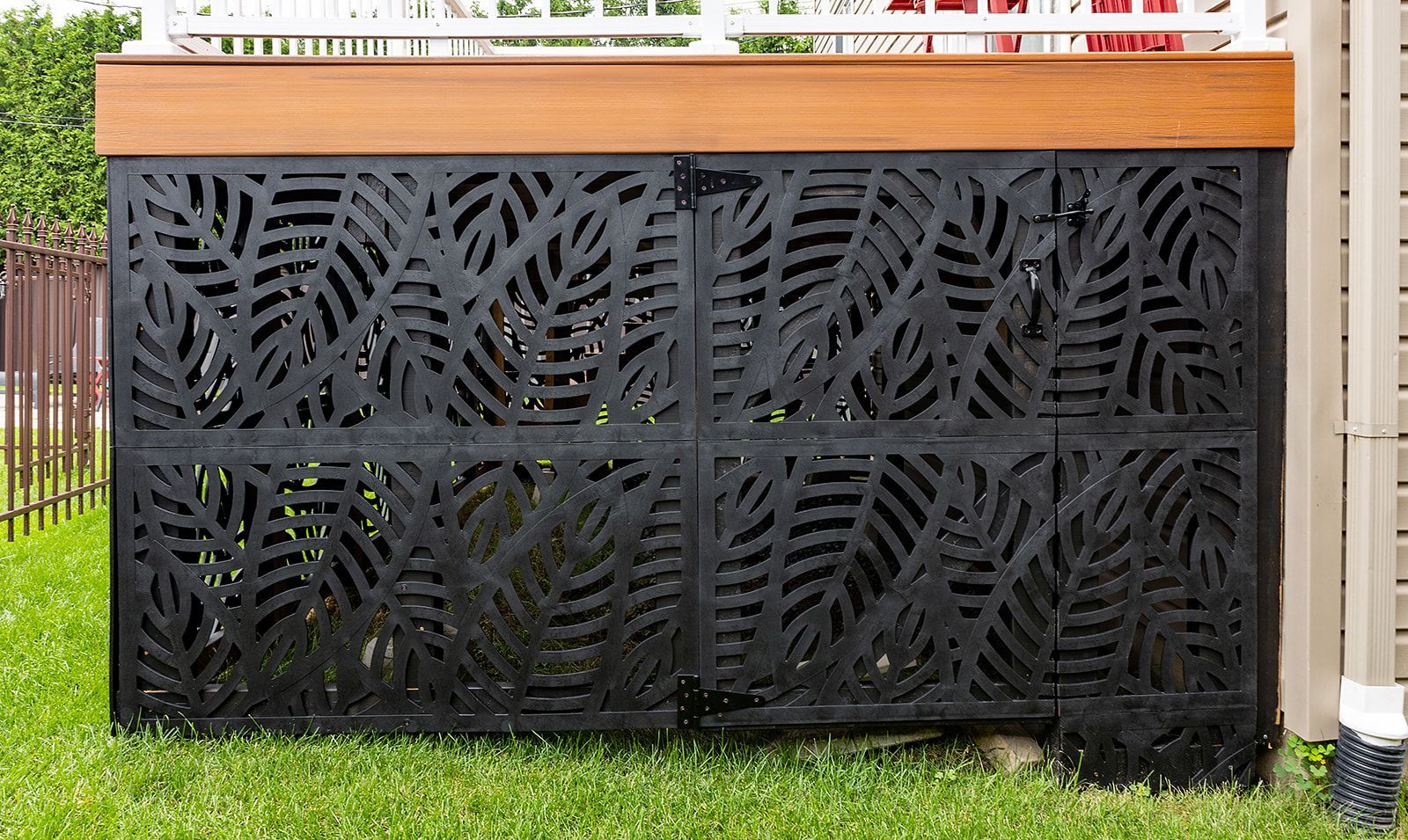Panneau décoratif en métal noir à motif de feuilles sous une terrasse en bois.