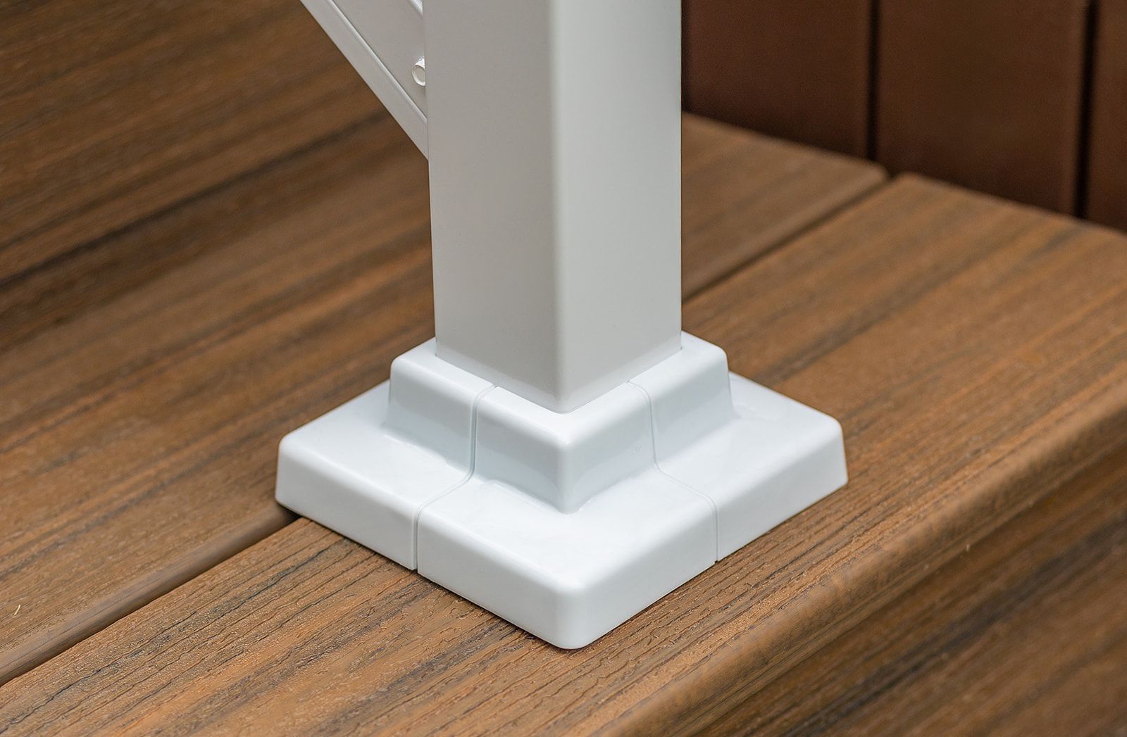 Socle blanc sur une terrasse en bois composite. Gros plan révélant un motif carré et étagé sous la lumière du soleil.