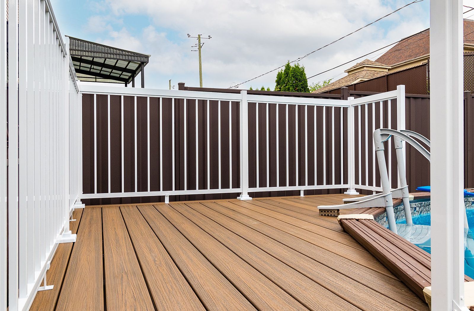Terrasse de piscine clôturée, marron et blanche, avec terrasse en composite et panneaux de bardage marron.