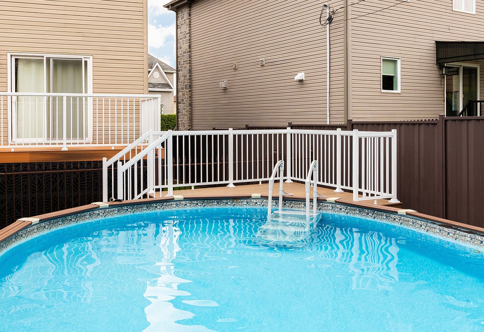 Piscine hors sol avec clôture de sécurité blanche, marches et maisons en arrière-plan.