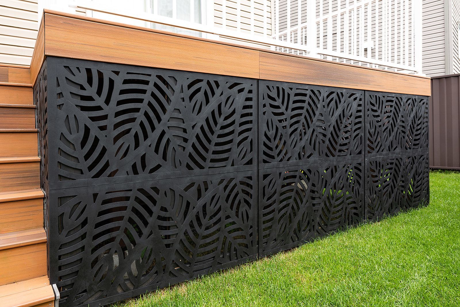 Panneaux décoratifs noirs découpés en forme de feuilles sous une terrasse en bois sur une pelouse.