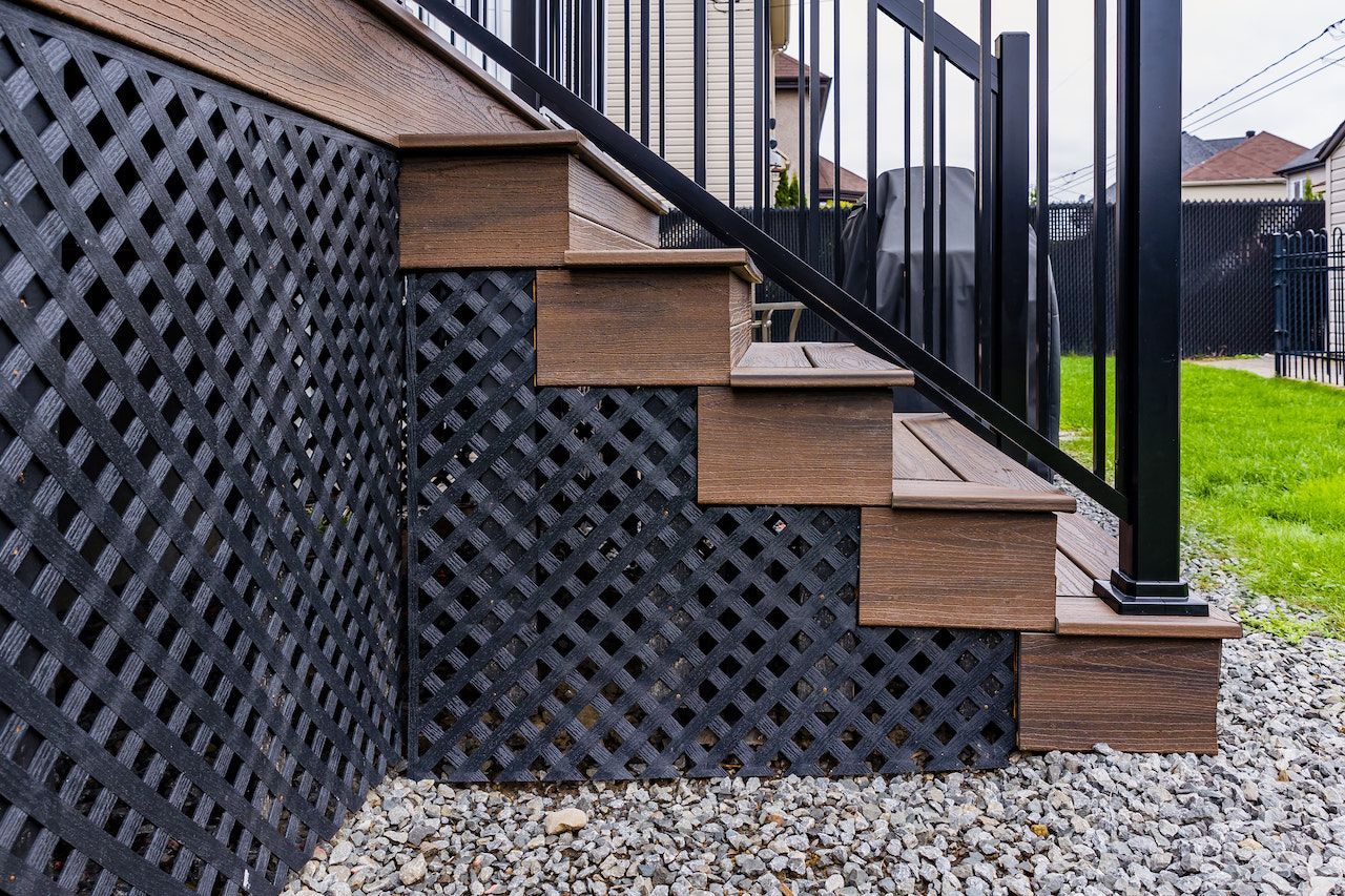 Escalier composite marron avec plinthe en treillis noir et rampe en métal noir, base en gravier.