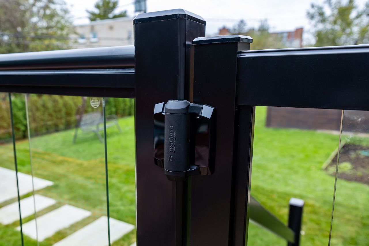 Rambarde de terrasse en métal noir avec panneaux de verre, dans un jardin.