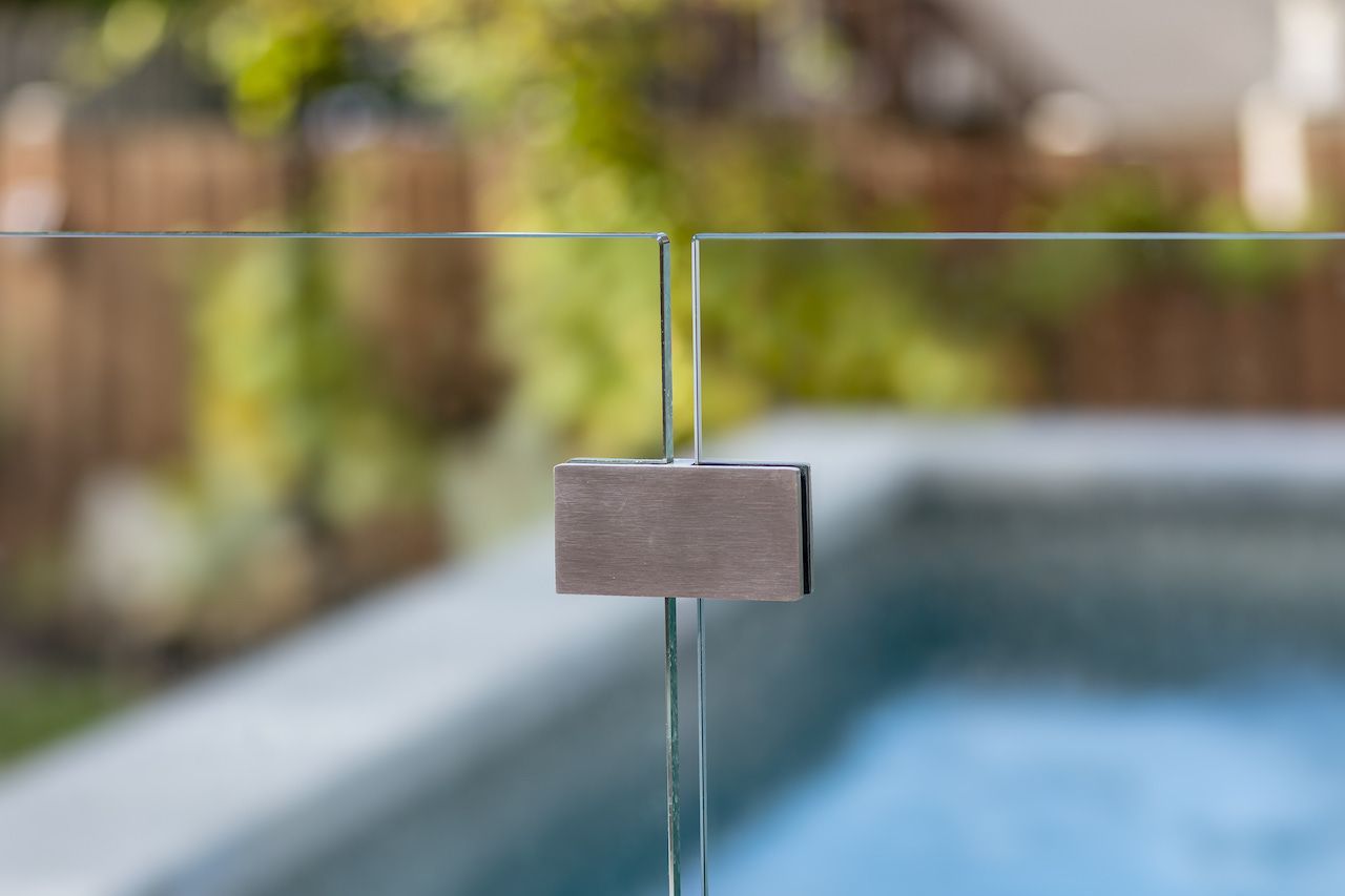 Clôture de piscine en verre avec un bloc de connexion aux tons neutres sur un fond vert flou.