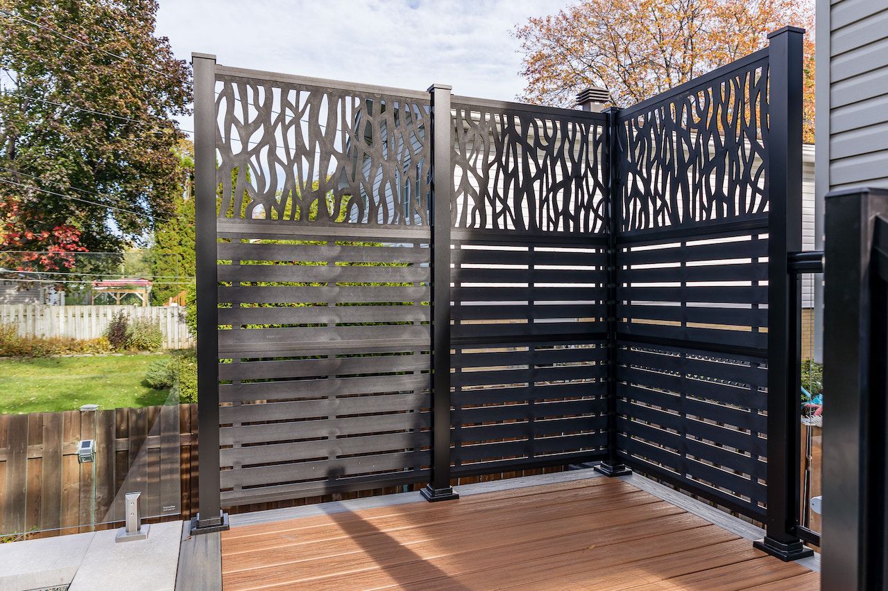 Paravent noir sur une terrasse en bois. Un panneau est orné de branches d'arbre, les autres sont composés de lattes horizontales. Aménagement extérieur.