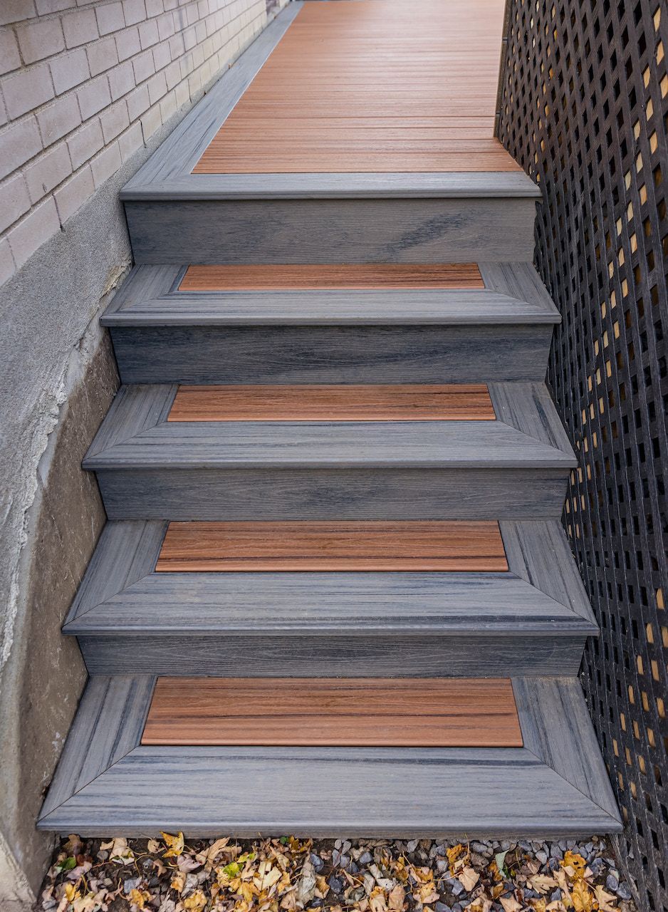 Escalier extérieur avec marches grises et éléments en bois brun menant à une terrasse en bois.