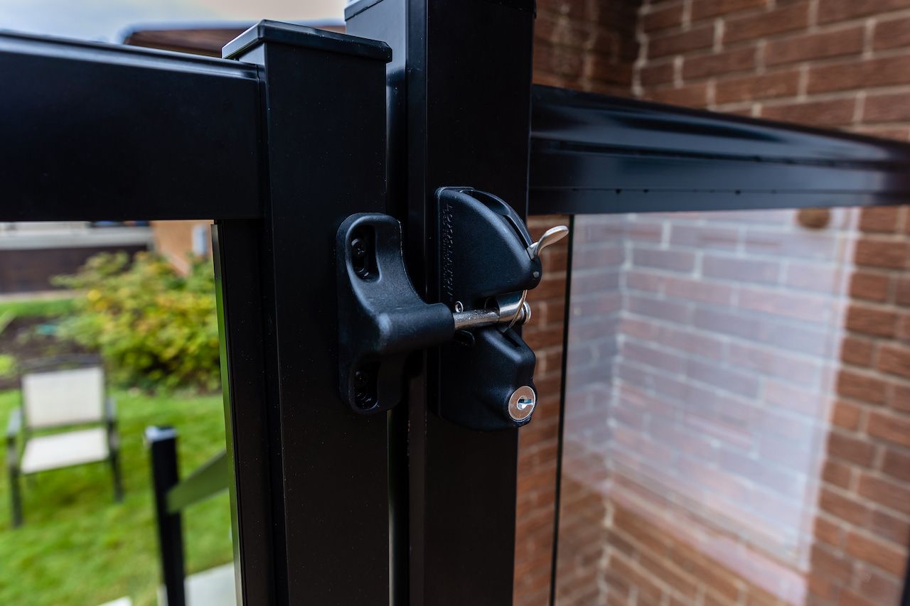 Loquet de portail noir sur un cadre en métal noir, avec serrure à clé, à côté d'un panneau de verre.