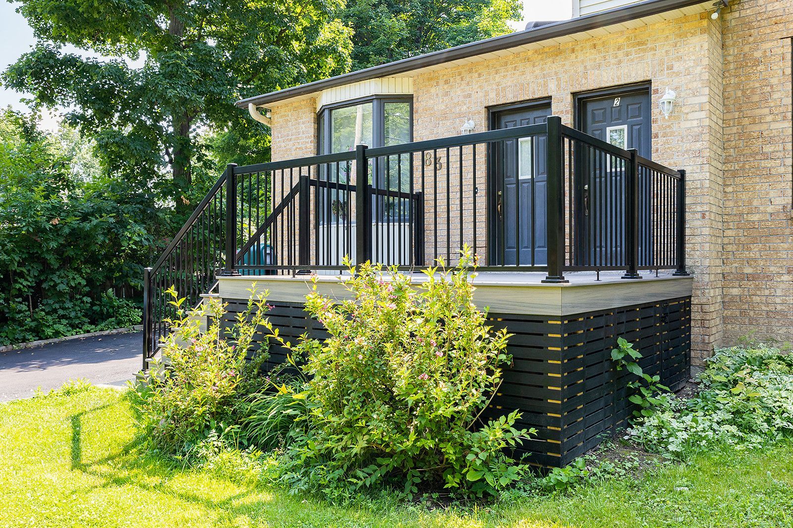 Terrasse noire avec rambarde devant un bâtiment en briques, entourée de verdure.