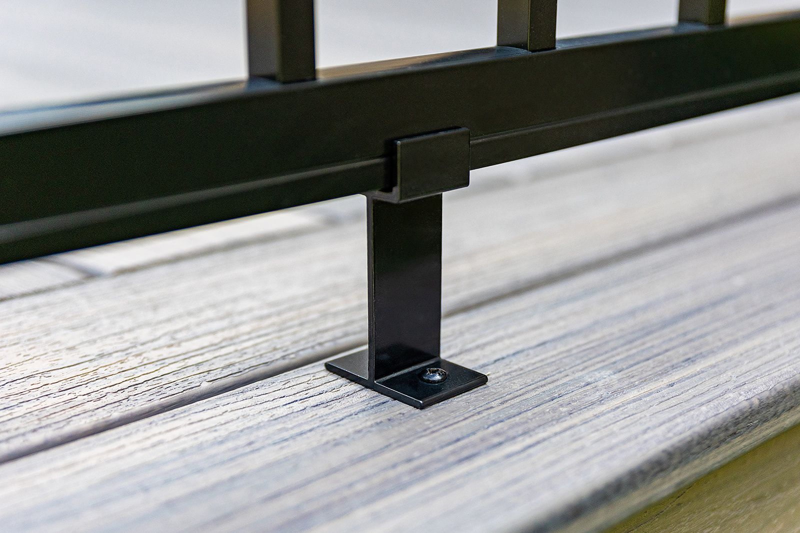 Poteau de rambarde en métal noir boulonné à des planches de terrasse gris clair.