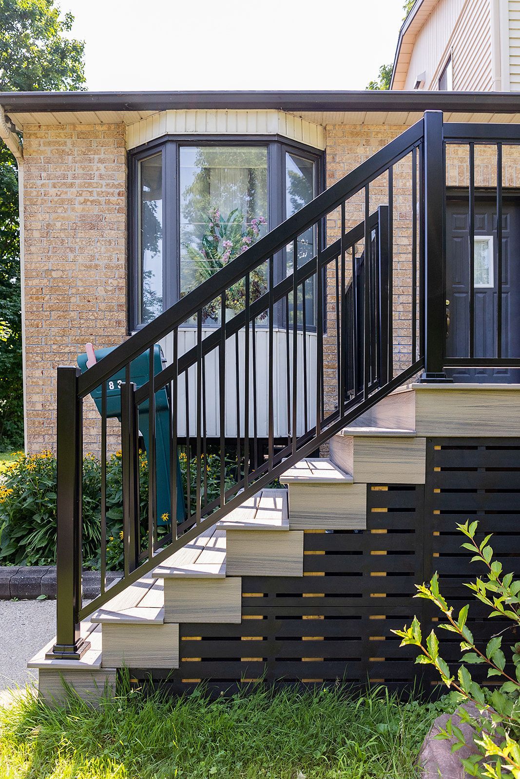 Rambarde en métal noir le long d'un escalier extérieur menant à une maison en briques avec une baie vitrée.