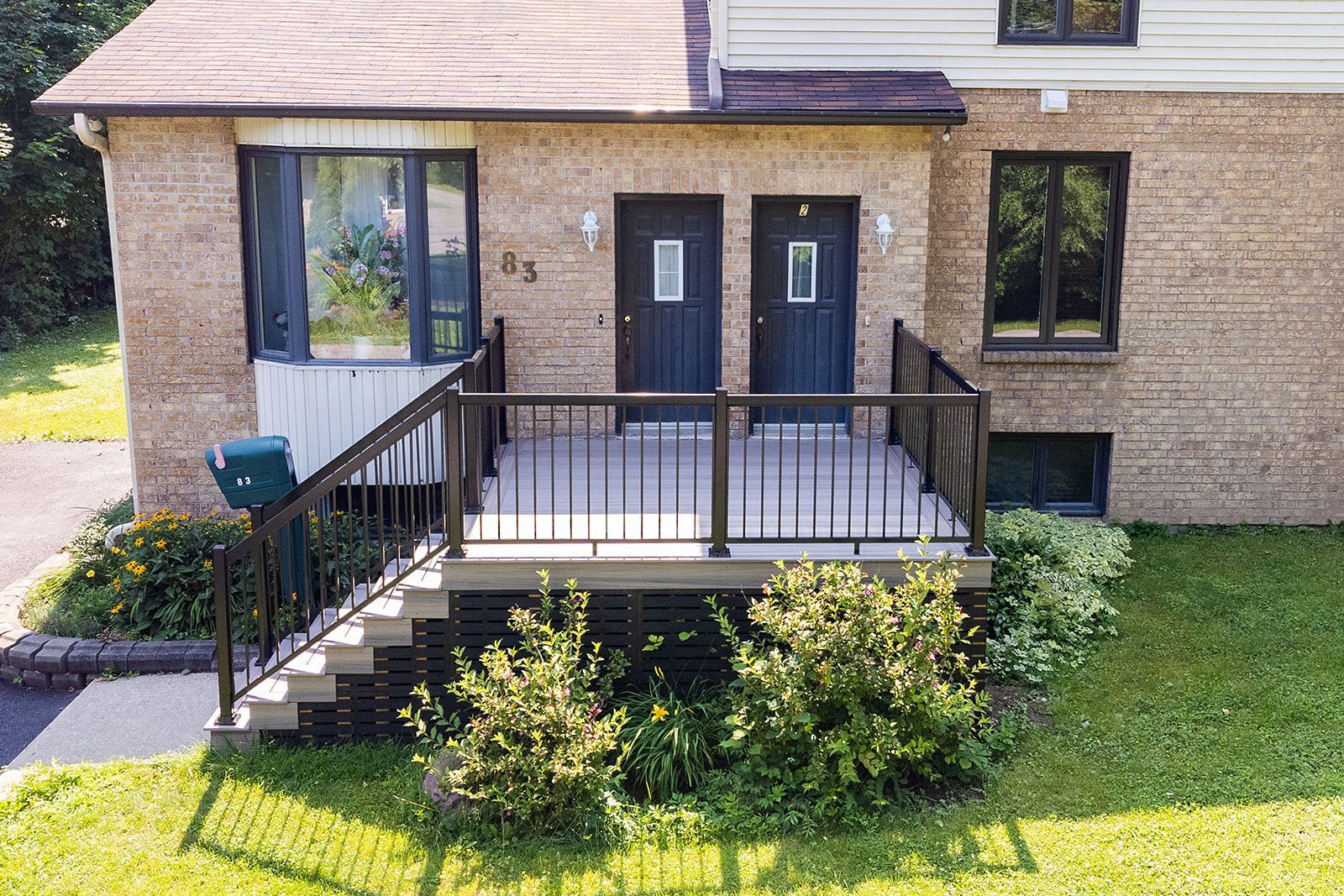 Extérieur de maison de ville avec deux portes, terrasse avec rambarde et aménagement paysager.