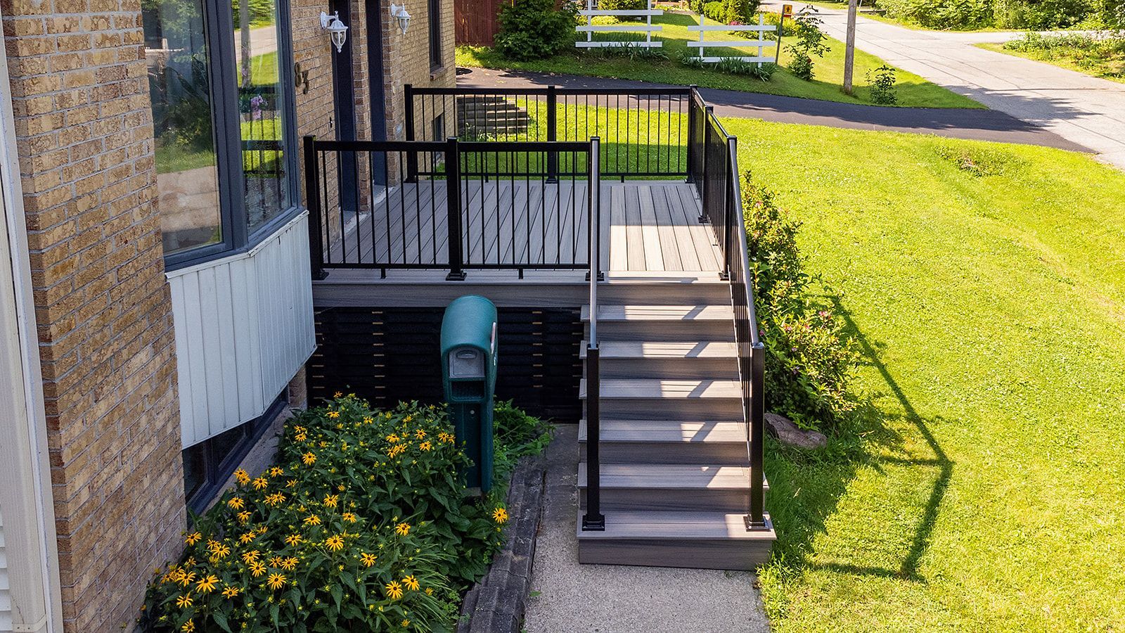 Une terrasse et un escalier attenants à un bâtiment, avec des rambardes noires, des marches grises et une cour gazonnée.
