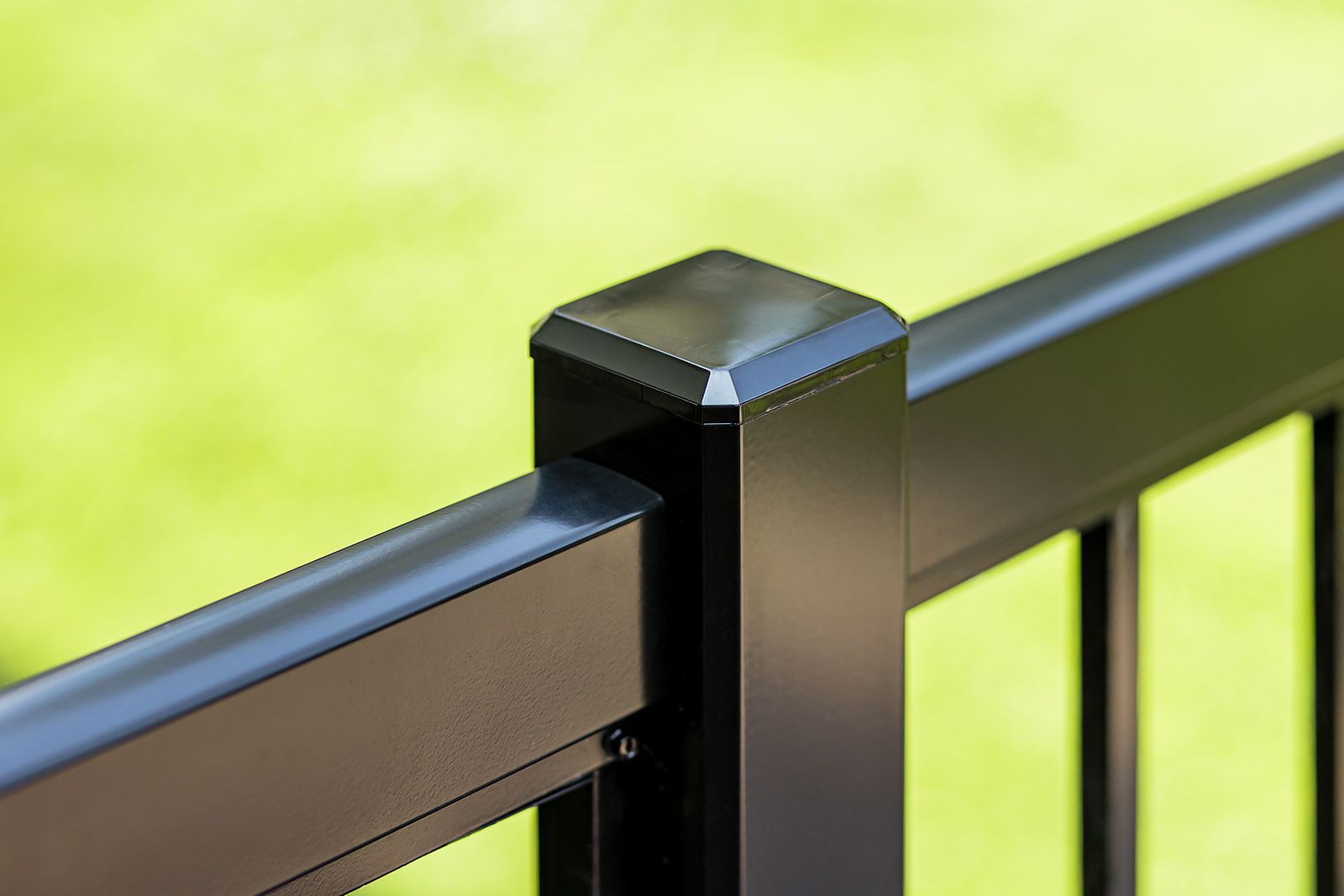 Rambarde de terrasse en métal noir avec un chapeau de poteau carré sur un fond vert flou.