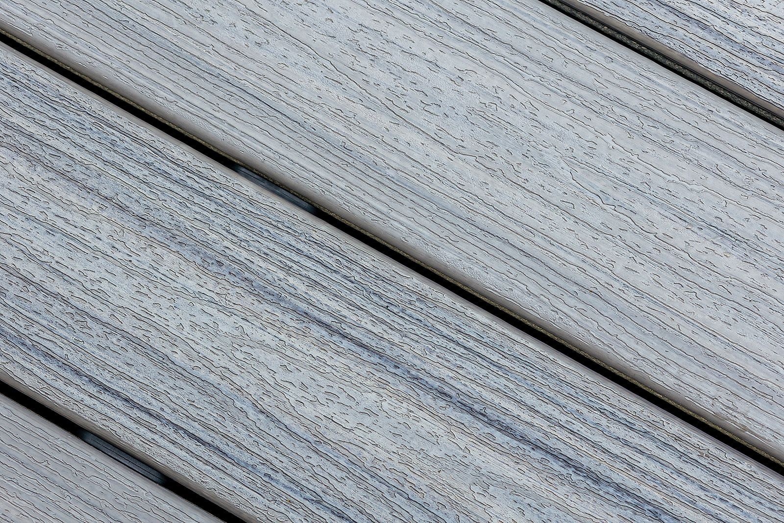 Lames de terrasse composites gris clair inclinées avec rainures foncées.