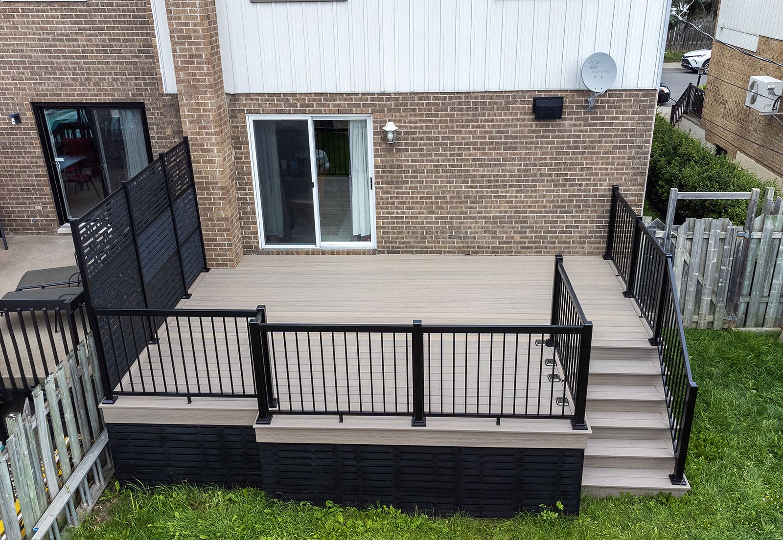Terrasse en composite avec rambarde et marches noires, adossée à une maison en briques.
