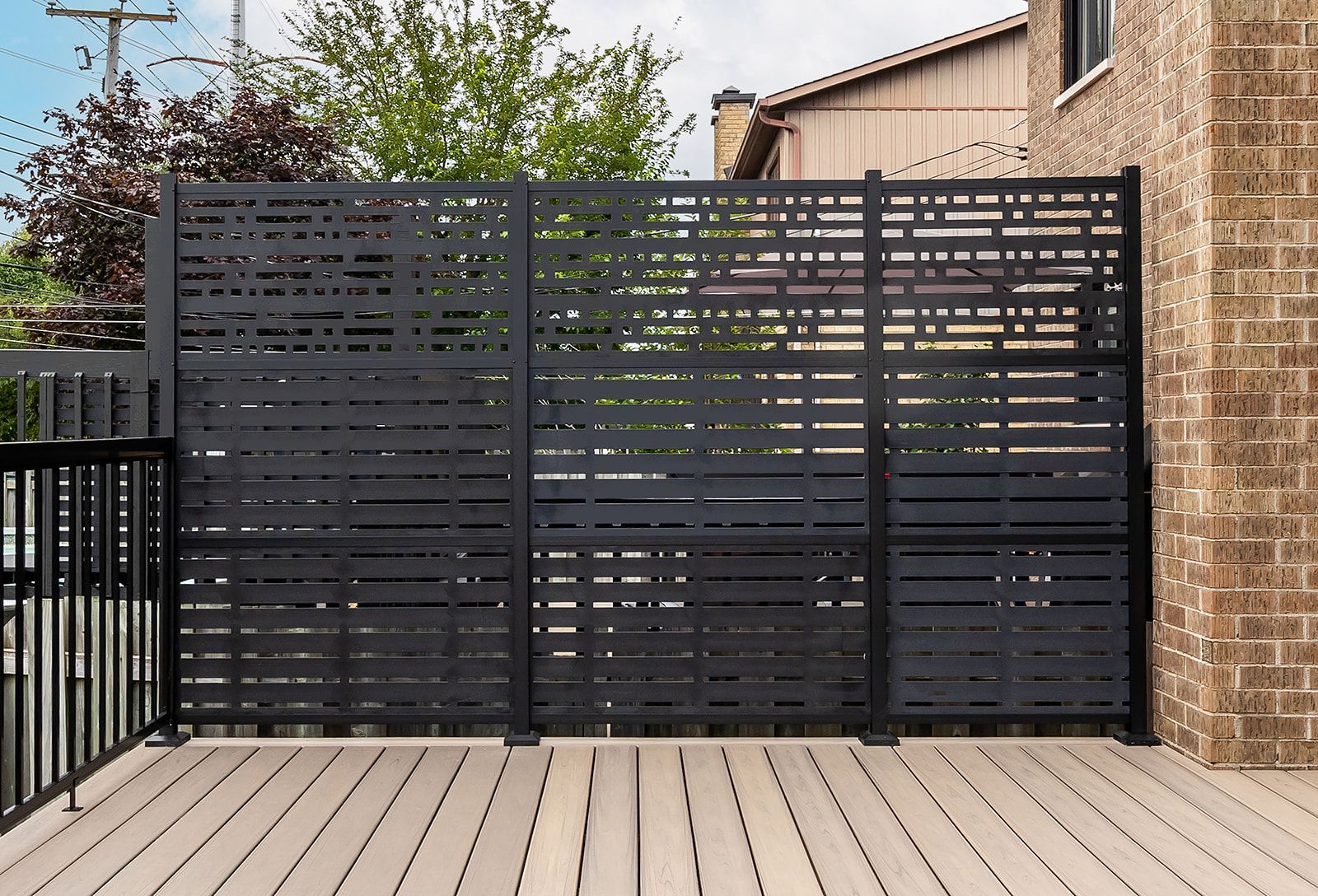 Clôture noire assurant l'intimité d'une terrasse en bois jouxtant un bâtiment en briques.