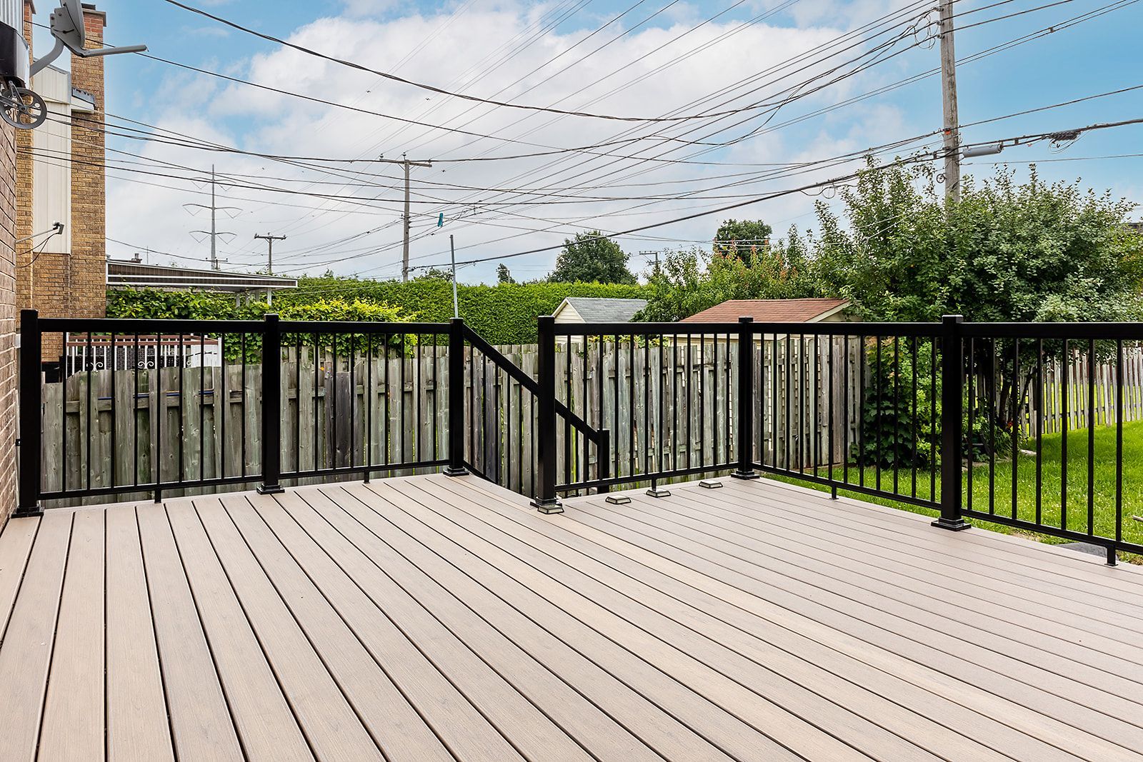 Terrasse arrière avec balustrades noires et parquet clair, donnant sur une clôture en bois et de la verdure.