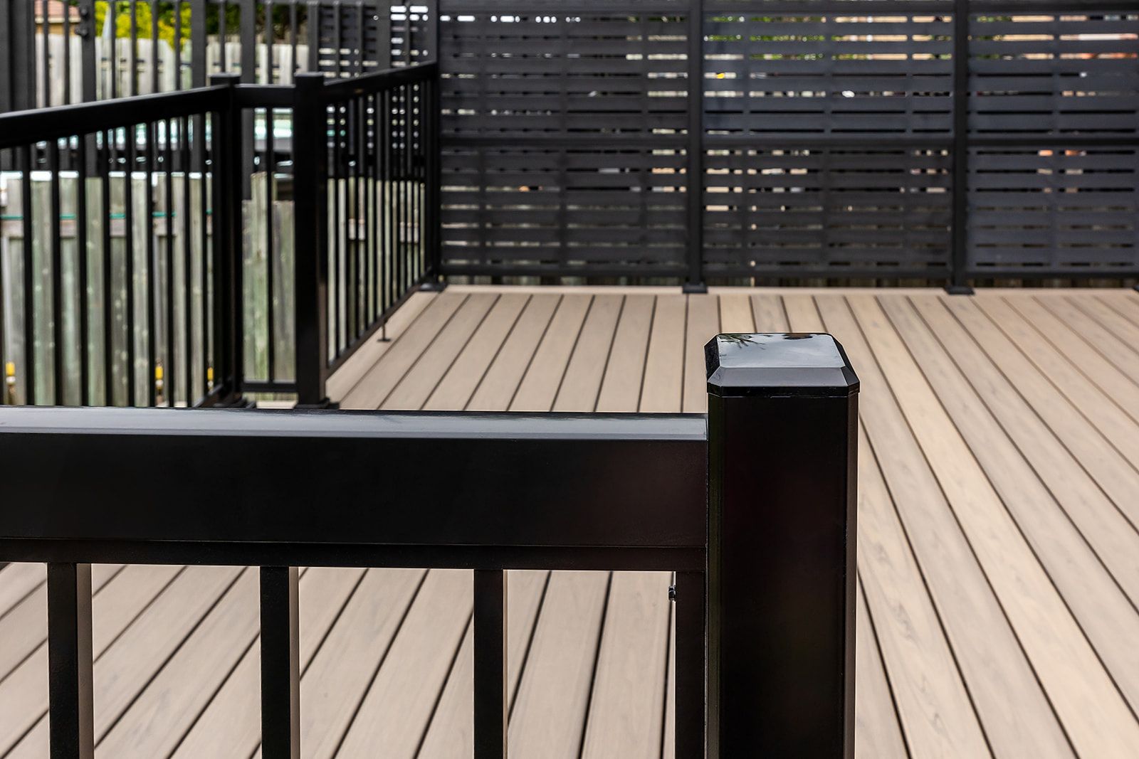 Rambarde et terrasse noires sur une terrasse en bois avec un paravent à lattes sombres pour plus d'intimité.