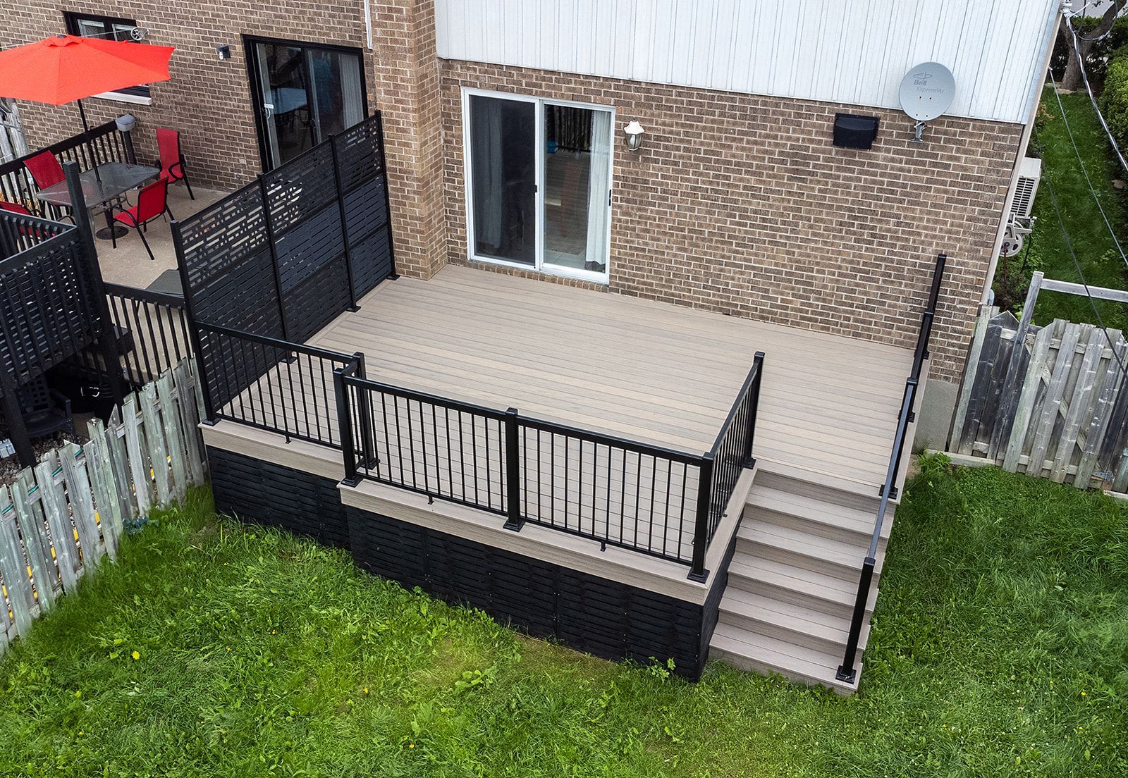 Une terrasse surélevée en composite avec des rambardes et un escalier noirs, dans un jardin gazonné.