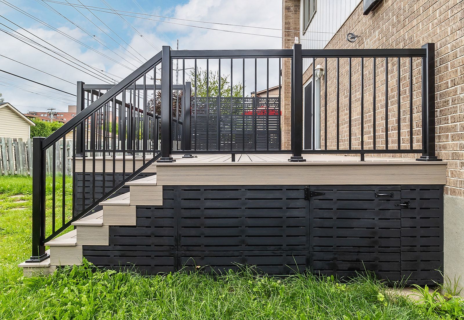 Terrasse noire avec marches, rambarde et plinthes peintes en noir, adossée à un bâtiment en briques.