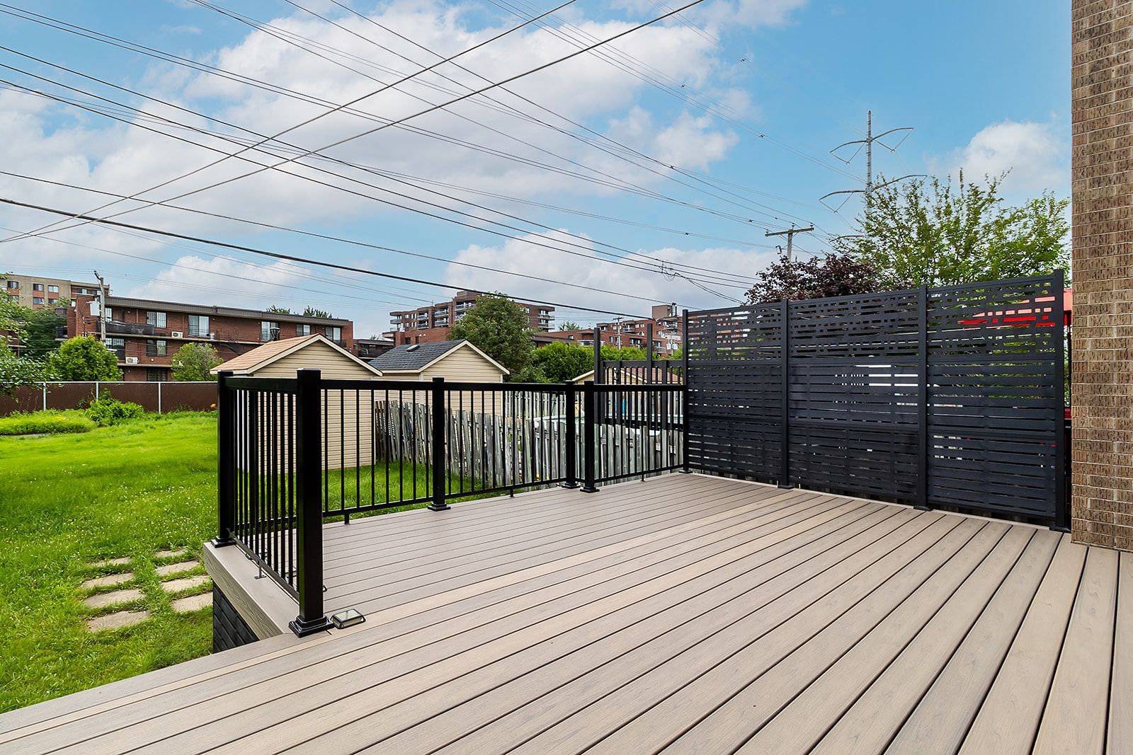 Terrasse en bois avec rambarde noire et brise-vue, donnant sur un jardin gazonné.