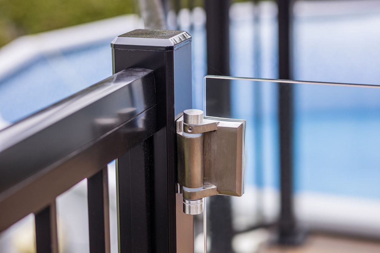 Rambarde en métal noir avec panneau de verre et charnière argentée, près d'une piscine.