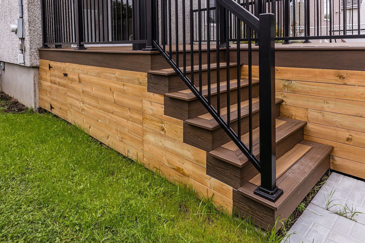 Escalier en bois avec rambarde noire et bardage en cèdre. Pelouse et allée en béton.