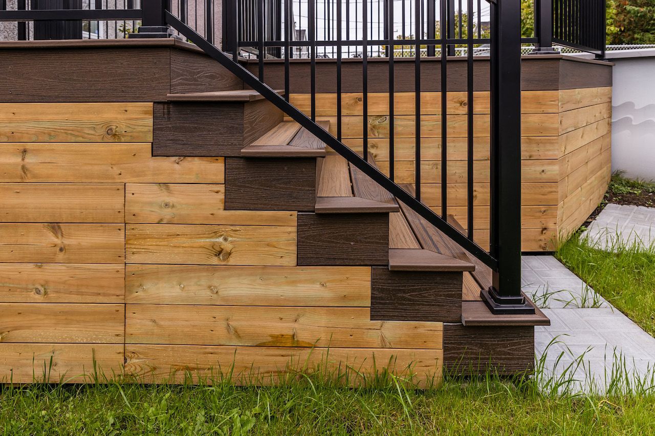 Escalier en bois avec rambarde noire et bardage brun clair, menant à une plateforme.